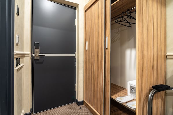 Habitación de hotel con puerta negra, armario de madera y baño pequeño con inodoro y barra para toallas.
