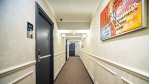 A hotel hallway with a carpeted floor, a door on the left, and a painting on the right wall. - Mildom City Hotel (Almaty)