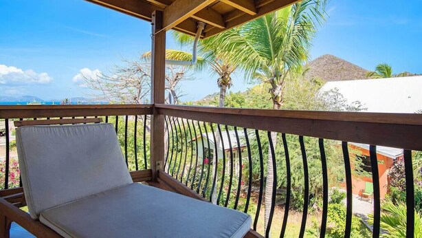 Un balcon avec un fauteuil rembourré, une rambarde en métal et une vue sur des palmiers et une montagne.