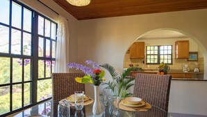 Un coin repas avec une table en verre, des chaises en osier et une vue sur la cuisine.