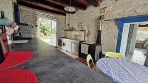 Una cocina rústica con lavadora, un fregadero y estufa. En primer plano, una mesa roja y una silla amarilla.
