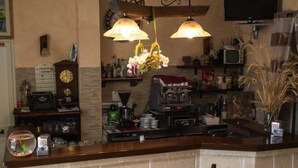 Uma cozinha com área de bar, apresentando um balcão de madeira, dois banquinhos, um relógio e uma televisão na parede.