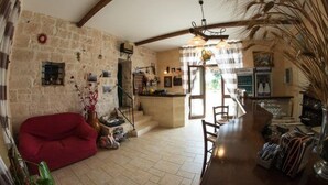 Um interior rústico com parede de pedra, sofá vermelho, balcão de madeira e escada que leva a uma varanda.