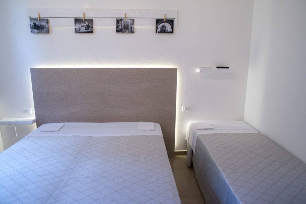Une chambre d’hôtel avec deux lits, une tête de lit, une table de chevet et une étagère murale ornée de photos.
