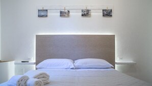 Quarto de hotel com uma cama grande, roupa de cama branca e cabeceira. Há três pequenas imagens na parede acima da cama.