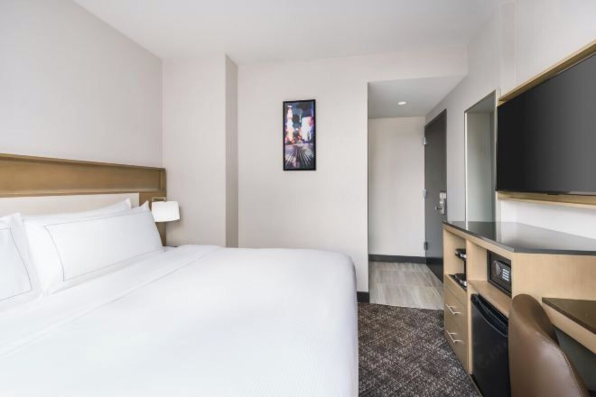 A hotel room with a bed, a desk, a television, and a door leading to a bathroom.