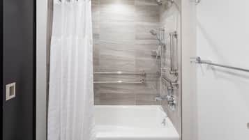 A modern bathroom with a bathtub, shower, and handrails.