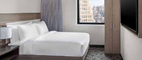 A hotel room with a large bed, a TV, a wardrobe, and a window with a city view.