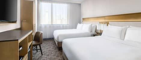 A hotel room with two beds, a desk, a chair, a television, and a large window with curtains.