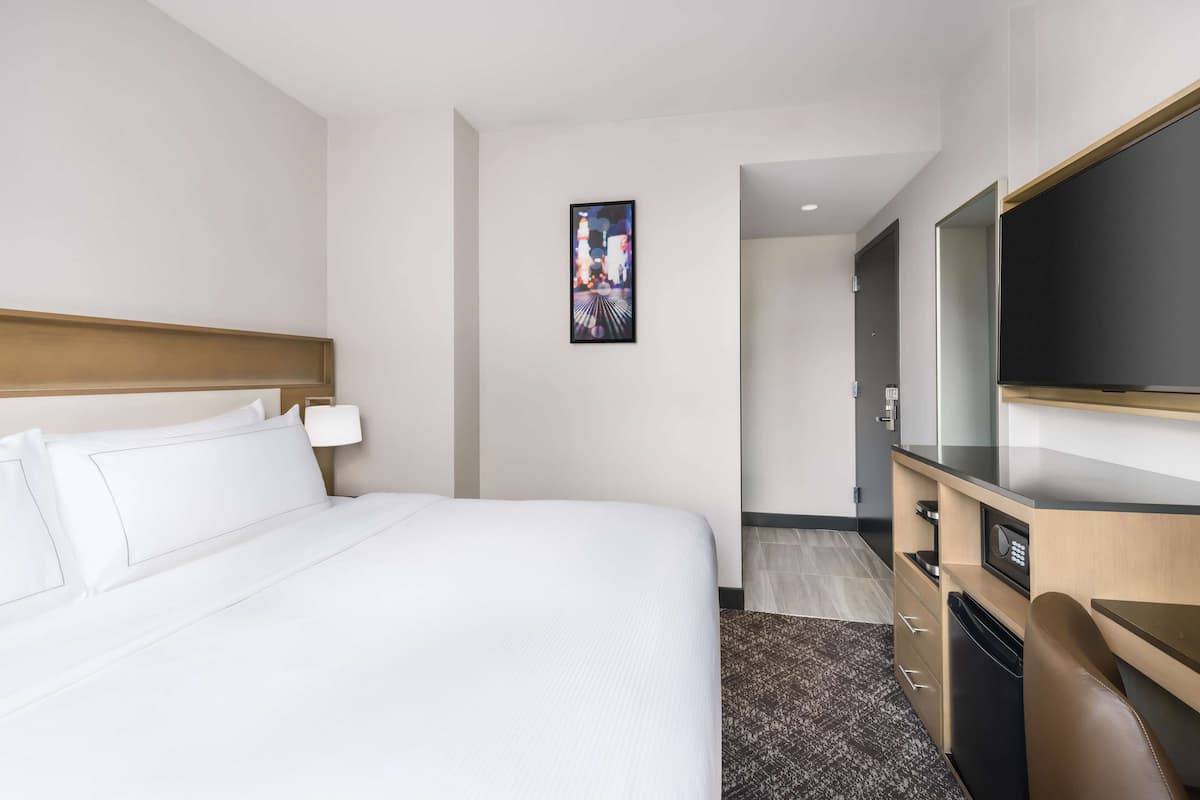 Ein Hotelzimmer mit einem Bett, einem Schreibtisch, einem Fernseher und einer Tür zu einem weiteren Raum.