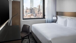 A hotel room with a bed, a desk, a chair, a TV, and a window with a city view. - Doubletree by Hilton New York Times Square South (New York)