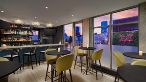 A bar area with a city view, tables, chairs, and a variety of bottles on shelves. - Doubletree by Hilton New York Times Square South (New York)