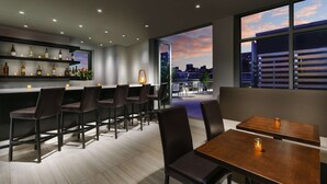 A modern bar area with a city view, bar stools, and a seating area with a table and chairs. - Doubletree by Hilton New York Times Square South (New York)