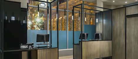 A modern hotel reception area with glass partitions, a reception desk, and a computer monitor.