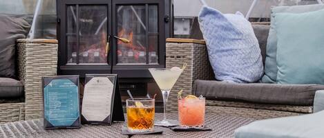A cozy outdoor seating area with wicker furniture, a menu, and two drinks on a table.