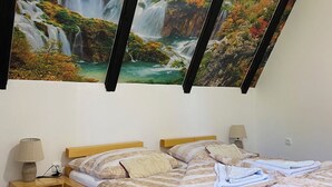 Un dormitorio con una cama de madera, una mesita de noche con lámpara, un tapete rayado de colores y un cuadro grande de una cascada en la pared.