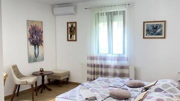 A bedroom with a wooden bed, a bedside table, a chair, a small round table, and a window with curtains.