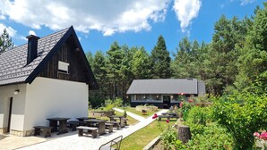 A rustic lodge with a white exterior and dark roof, surrounded by lush greenery and pine trees. - House Maka (Plitvicka Jezera)