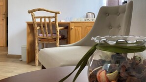 Un comedor con una silla de madera, una silla acolchada, una mesa con un cuenco de cristal con flores secas y un televisor de pantalla plana montado en la pared.