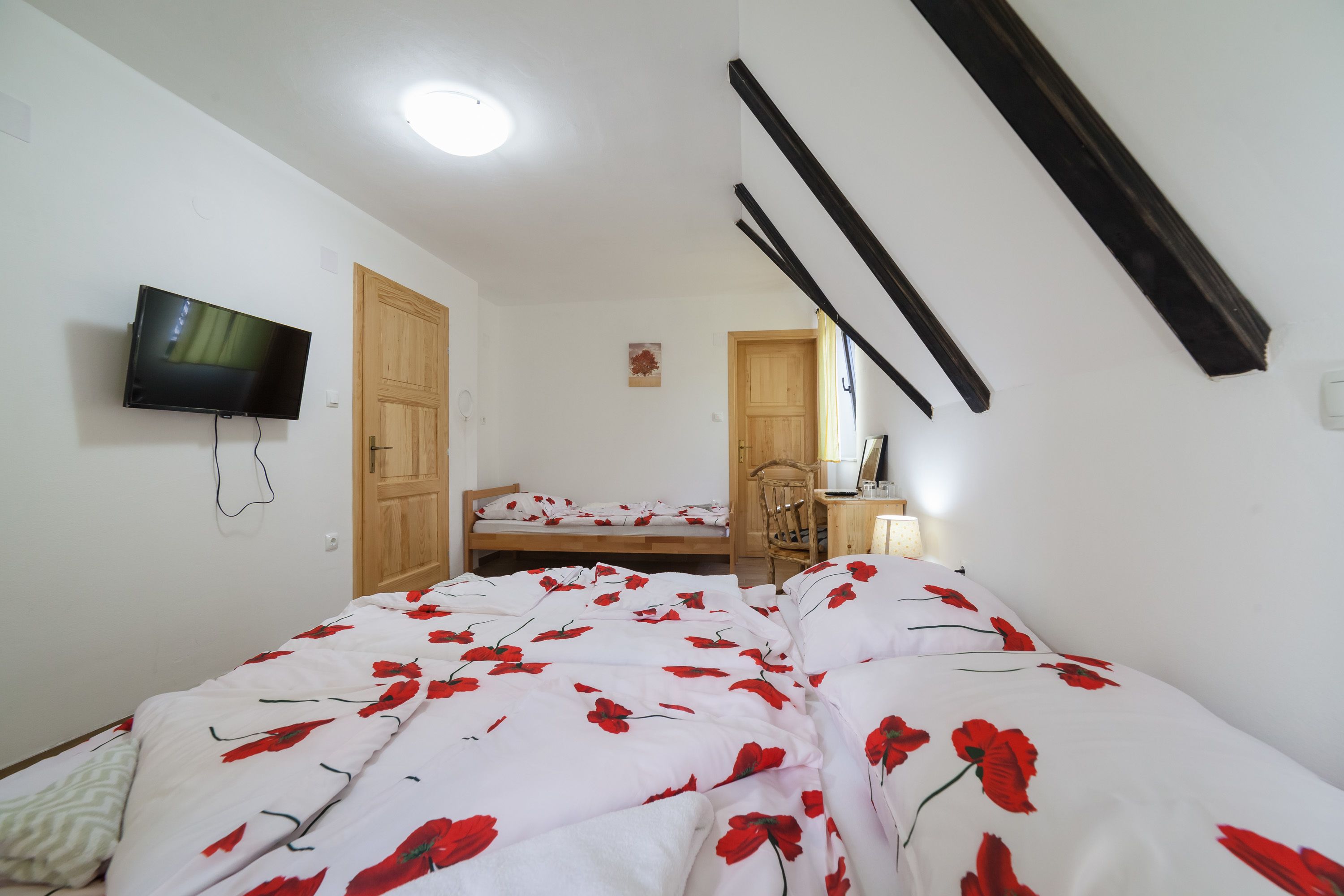 Une chambre à coucher avec un lit, un téléviseur fixé au mur, une porte en bois et un petit bureau avec une chaise.