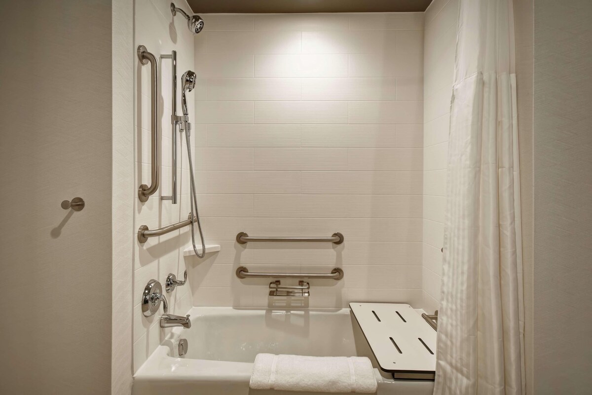 A bathroom with a bathtub, grab bars, a showerhead, and a towel rack.