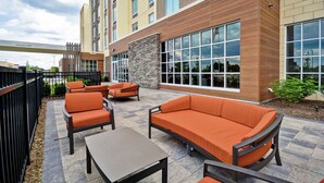 Ein Terrassenbereich im Freien mit orangefarbenen Sitzgelegenheiten und Steinböden, neben einem Gebäude mit großen Fenstern und einer Steinfassade.