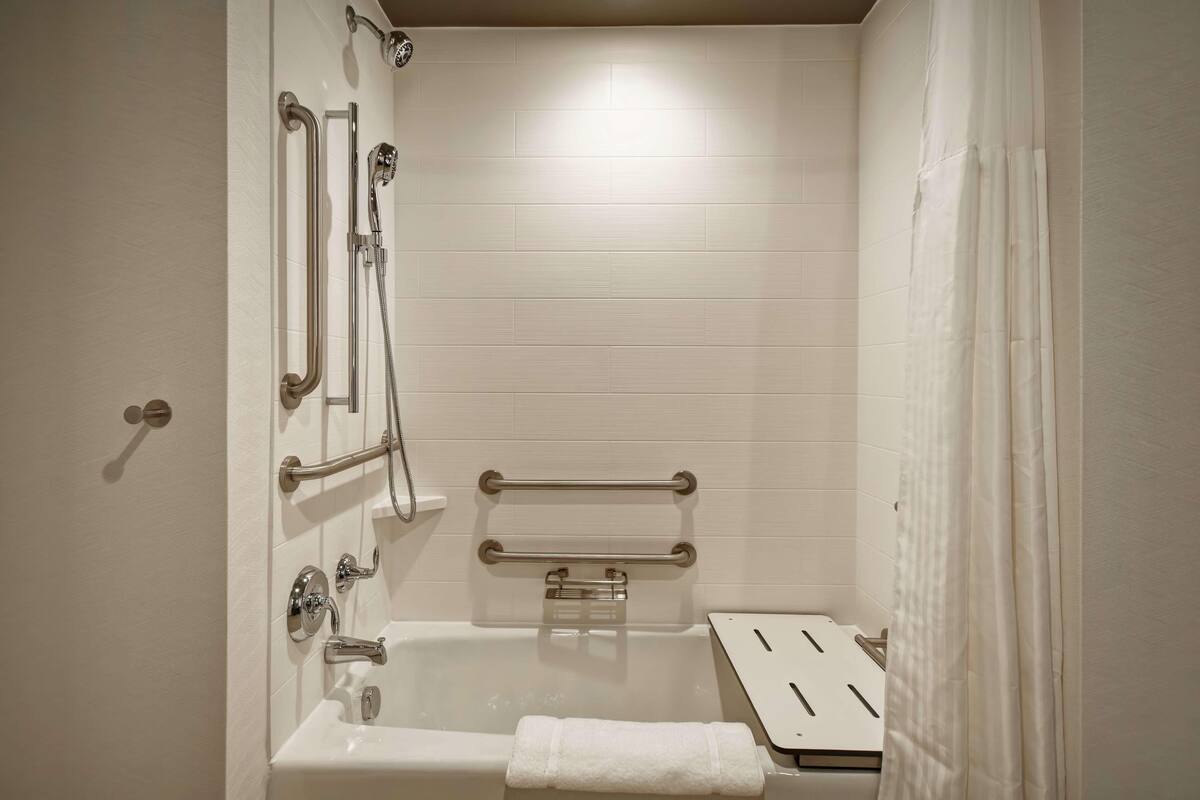 A bathroom with a bathtub, grab bars, a towel rack, and a showerhead.