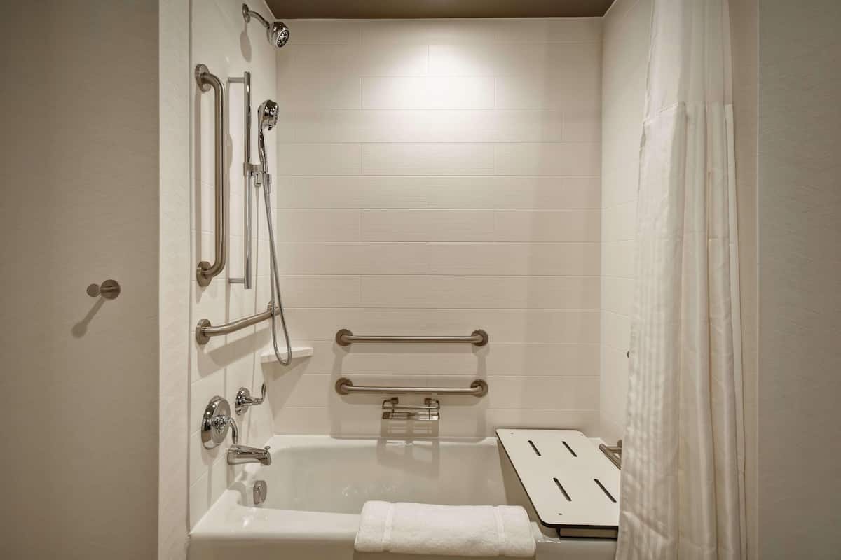 Ein Badezimmer mit Badewanne, Haltegriffen, einem Handtuchhalter und einer Duschbrause.