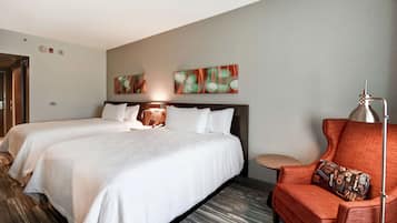 A hotel room with two beds, a red armchair, and abstract wall art.