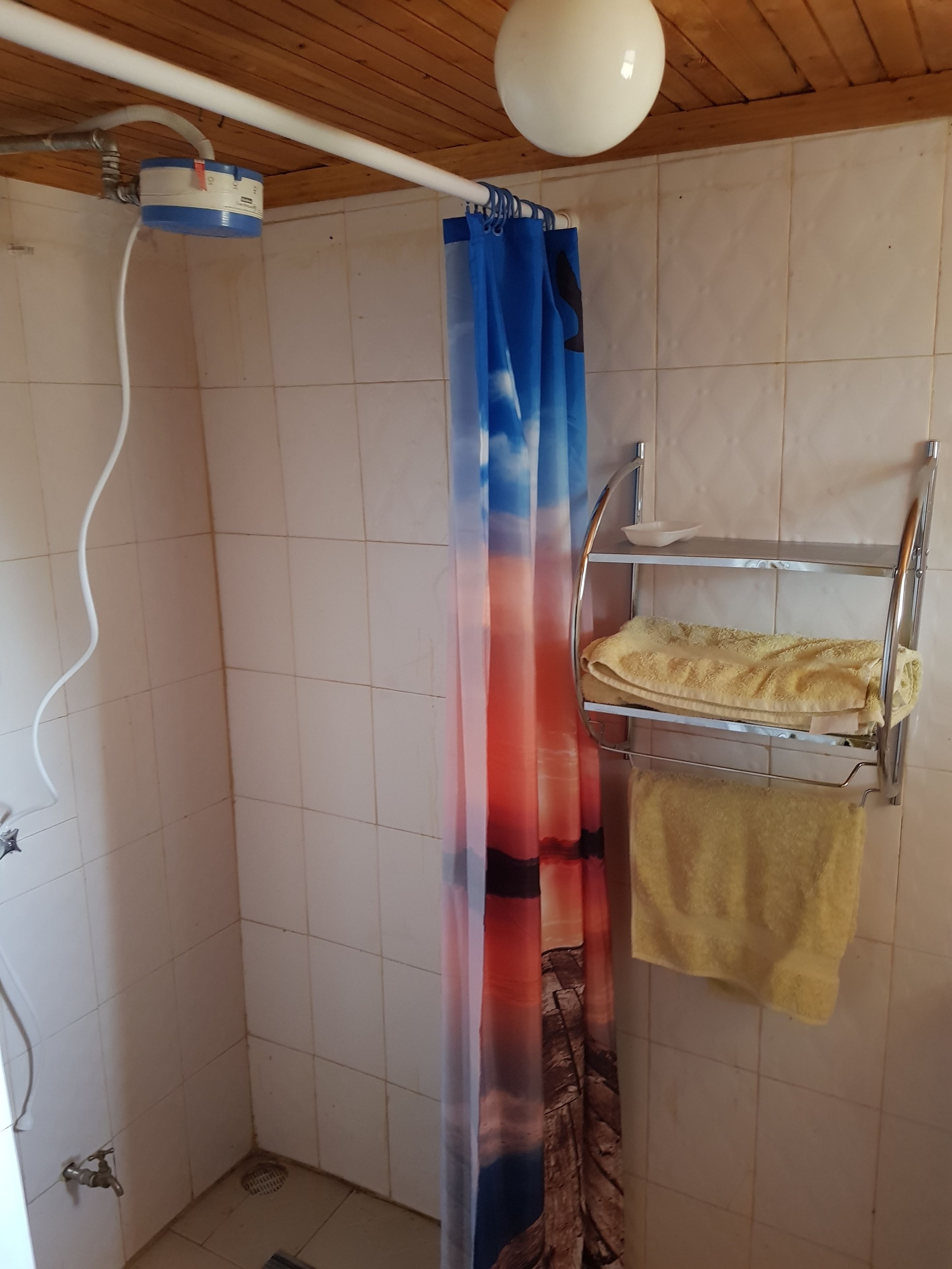 Un baño pequeño con azulejos, cortina de ducha, toallero y calentador de agua.