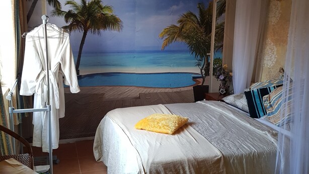 A bedroom with a beach mural, a bed with a yellow pillow, and a wooden ceiling.