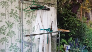 A bathroom with a shower area, a towel rack with a robe, and a pair of slippers.