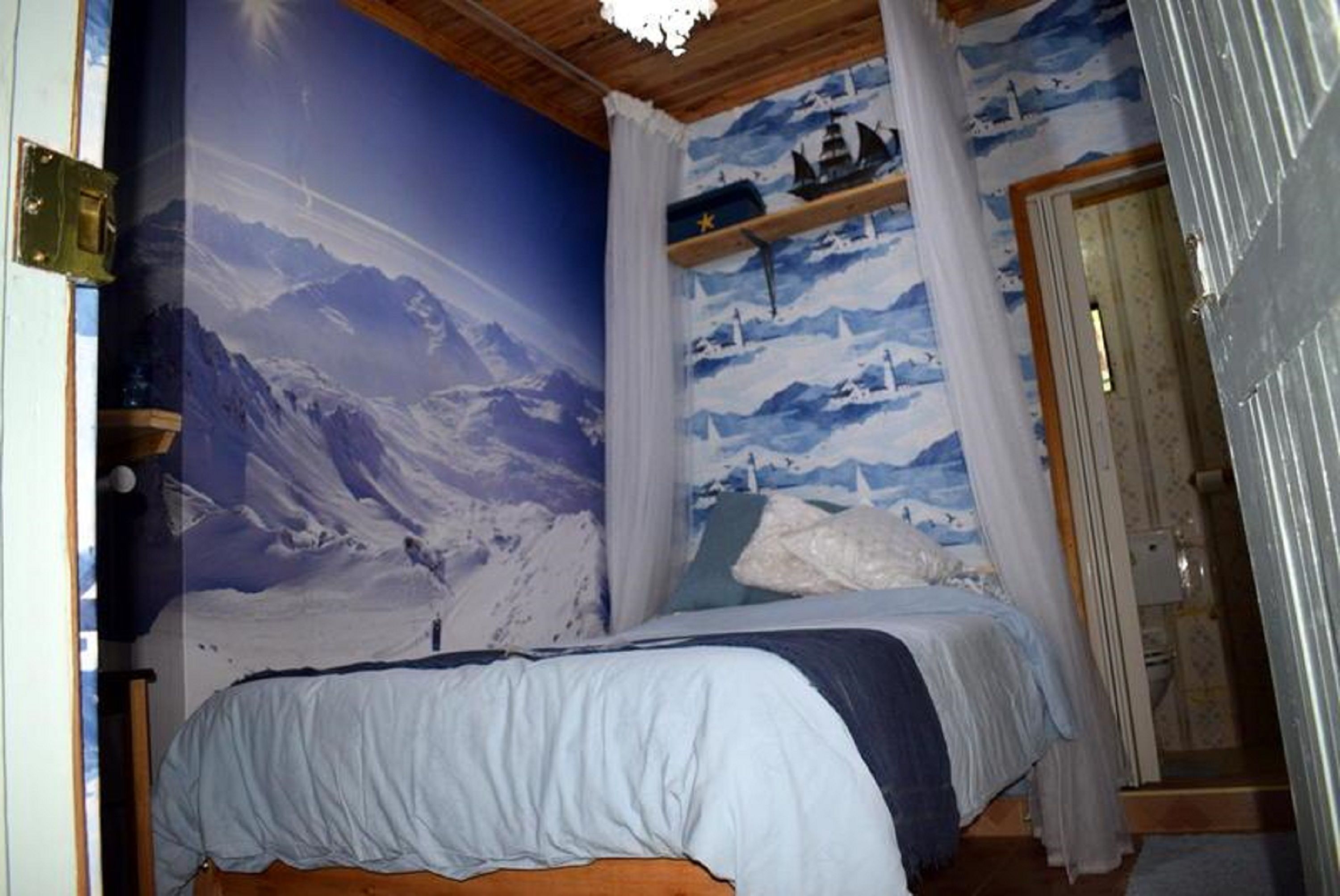 Ein Schlafzimmer mit einer Wandmalerei von einer Berglandschaft, einem Bett mit blauer und weißer Bettdecke und einem Holz-Kopfende.