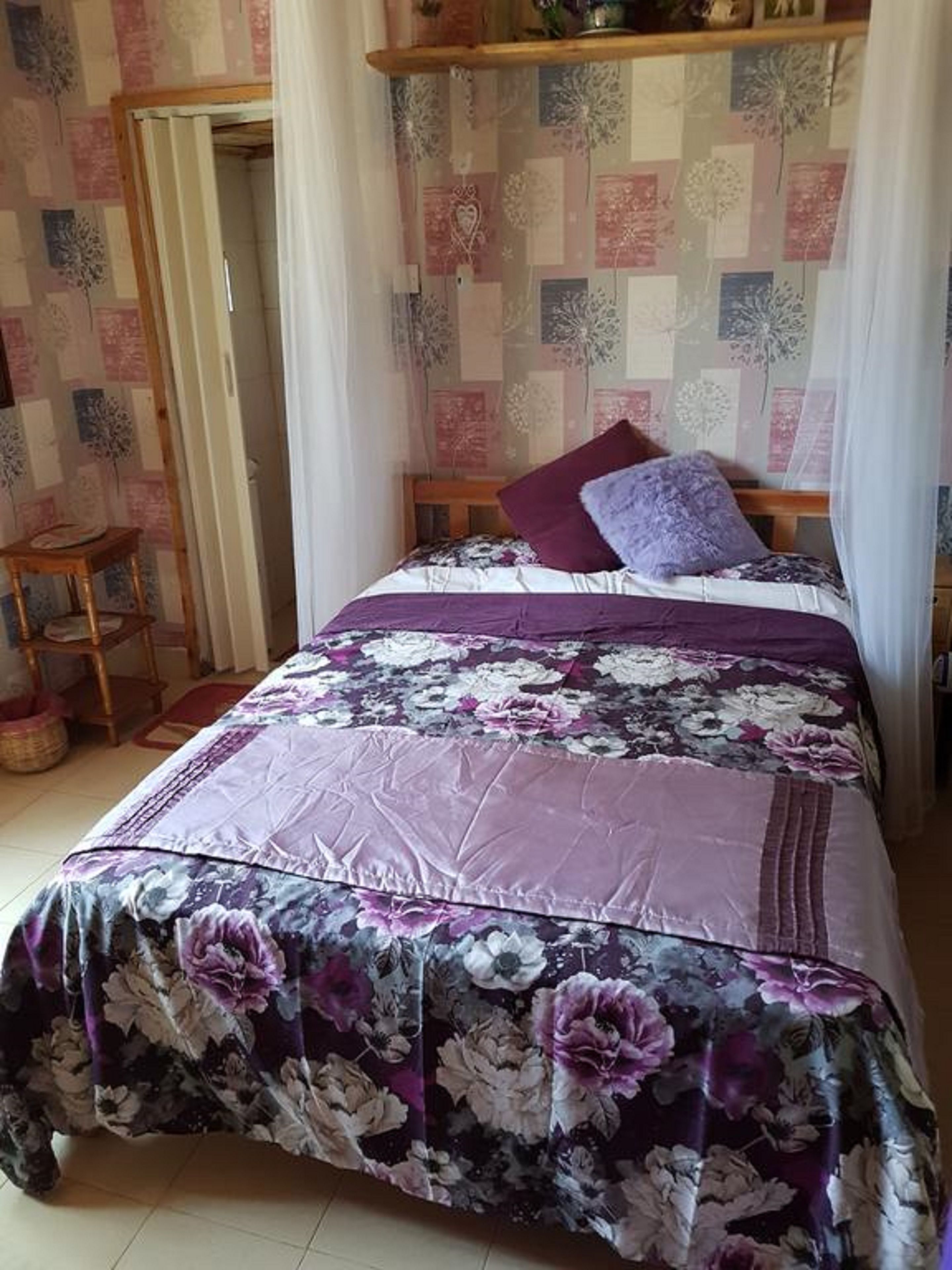 Een slaapkamer met een bloemenprint deken, een houten hoofdbord en een klein houten krukje.