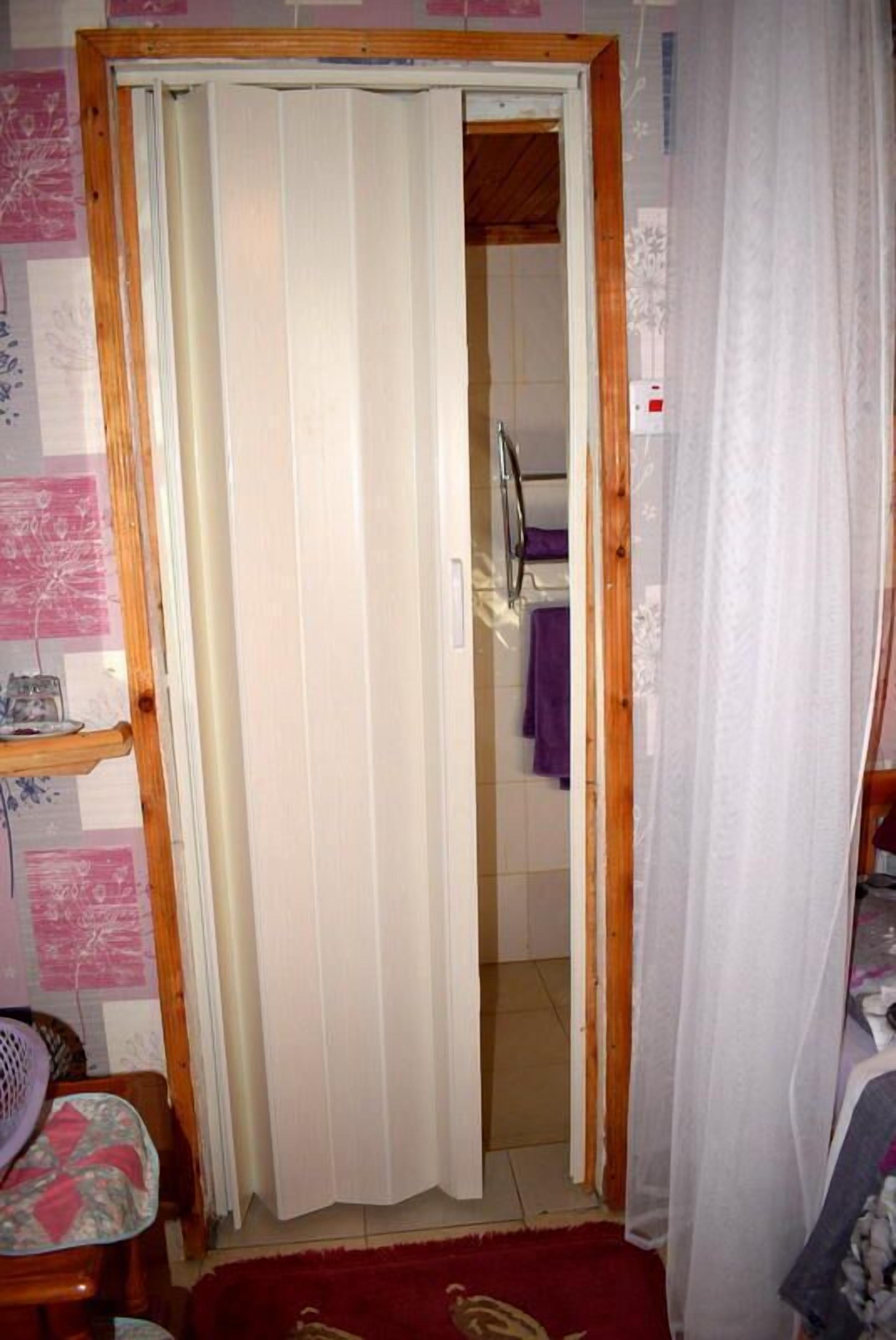 Una habitación con una puerta de madera, una alfombra roja y un baño visible a través de la puerta.