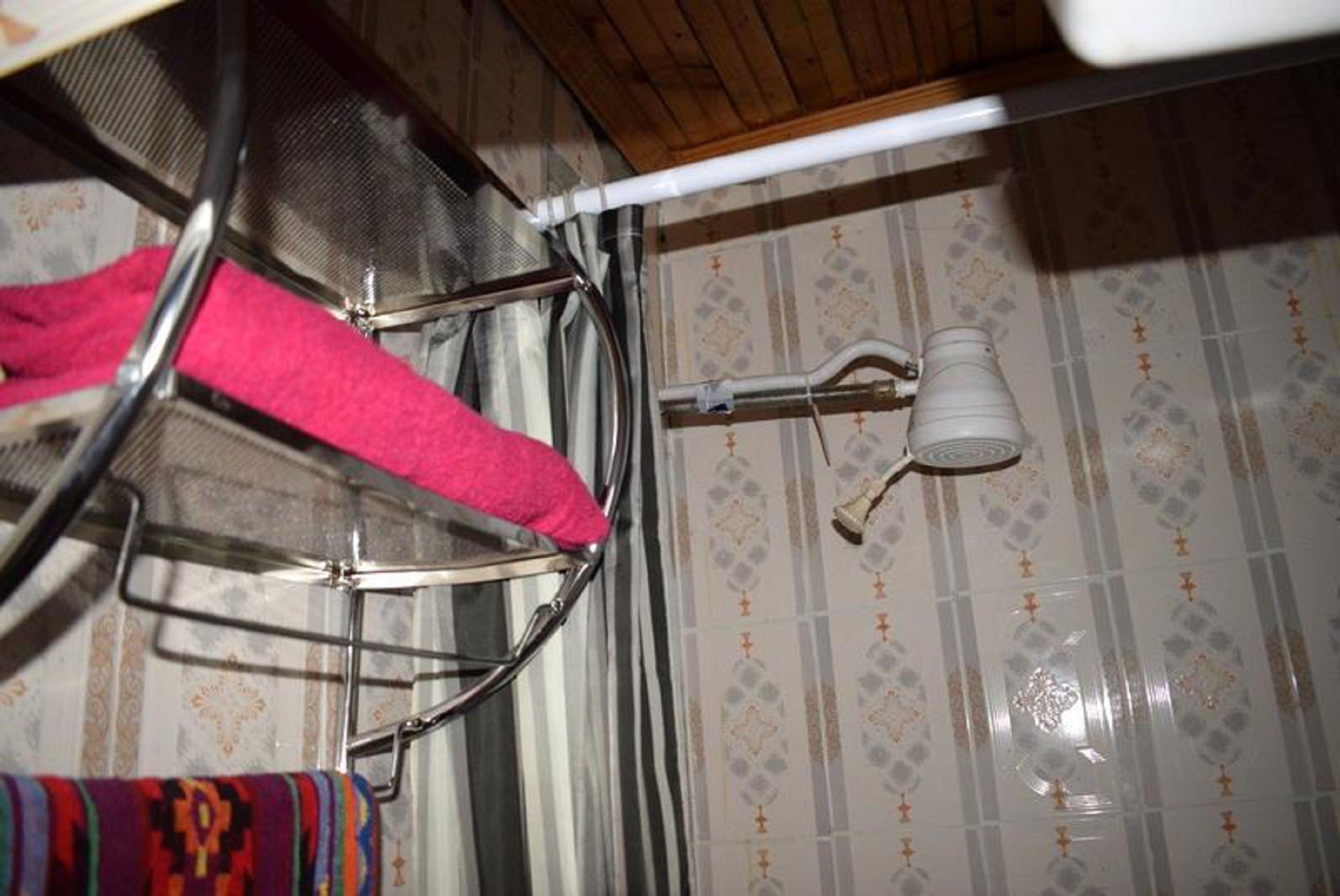 Un baño con un tendedero de metal, una toalla blanca y un cabezal de ducha.