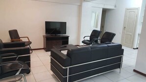Een moderne woonkamer met een zwarte leren bank, een televisie op een houten dressoir en twee zwarte fauteuils.