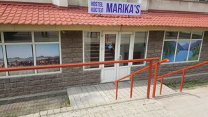 Een hostel genaamd MARIKA'S met een dak van rode tegels, grote ramen en een trap met oranje leuningen.