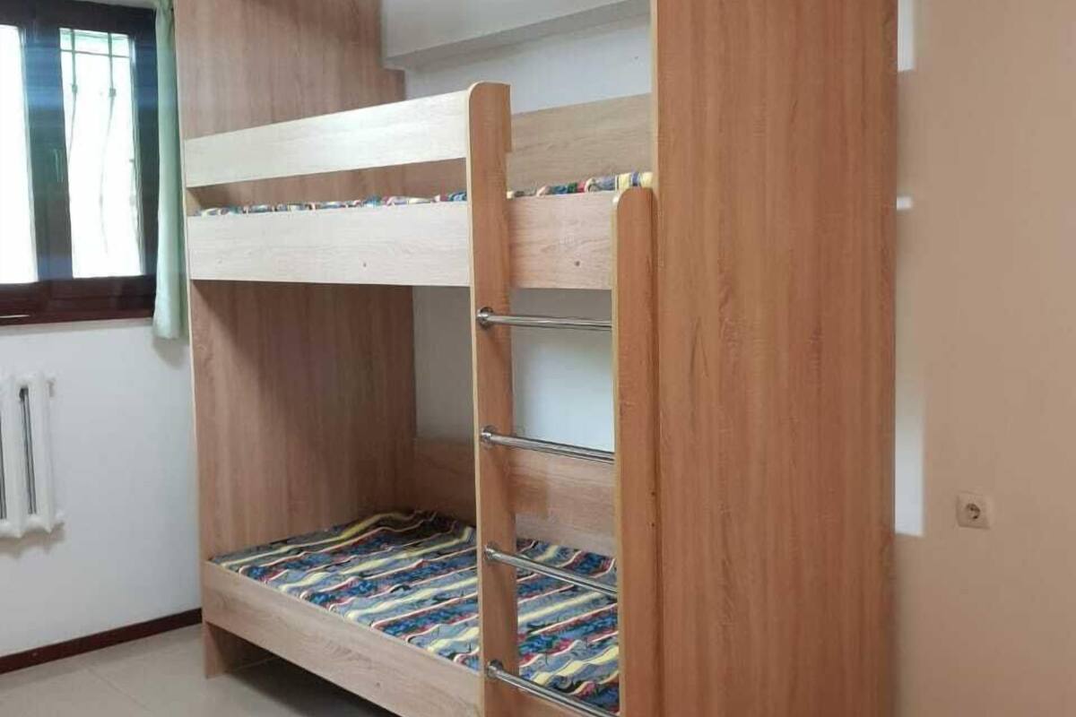 A bunk bed with a wooden frame and metal ladder, a window with curtains, and a radiator.