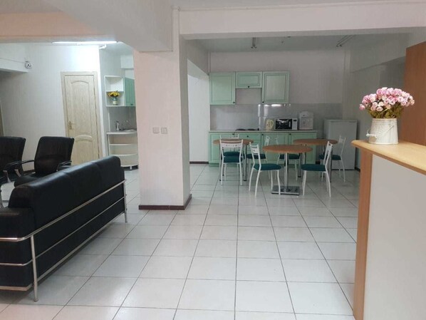 Un salón amplio con sofá, mesa de comedor y sillas. Se ve una cocina al fondo, con armarios verdes y un microondas.
