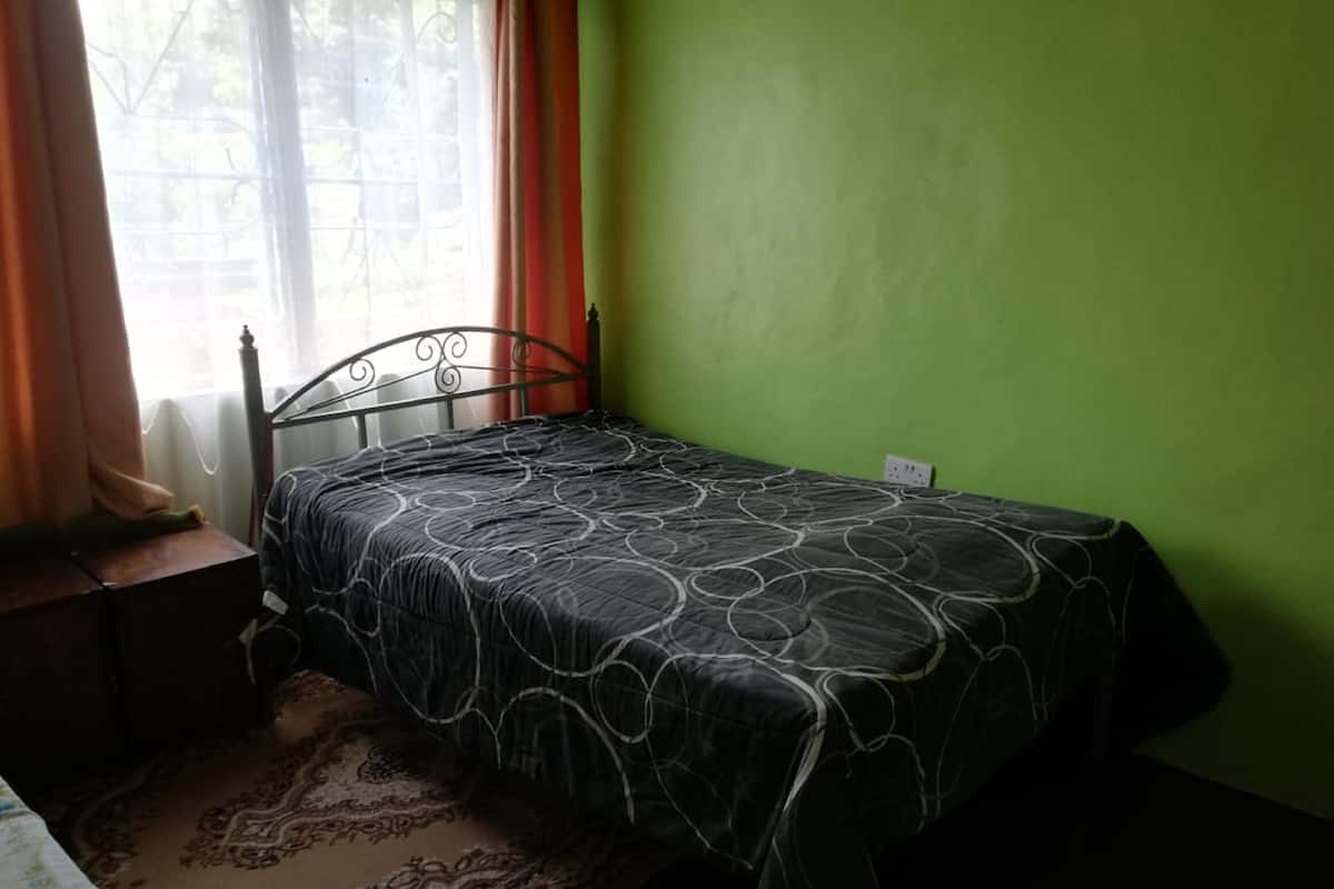 A small, single-bed room with a metal bed frame, a patterned bedspread, a wooden nightstand, and a patterned rug.