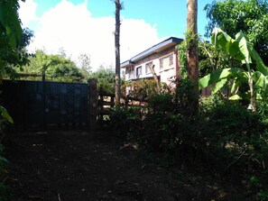 A gated area with dense vegetation and a building in the background. - Karugia House (Murang'a)