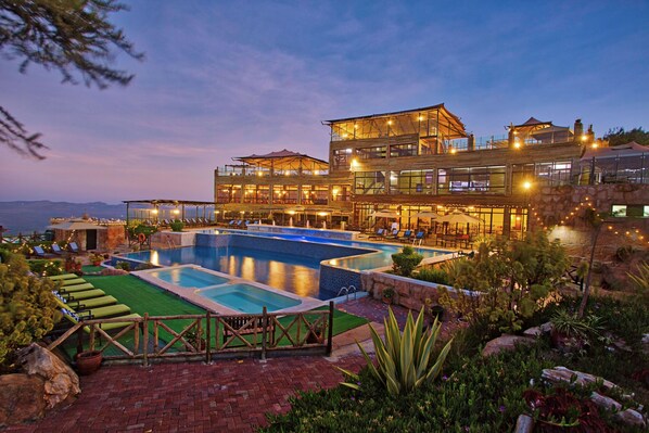 A multi-story hotel with a swimming pool, outdoor seating, and a view of the mountains.