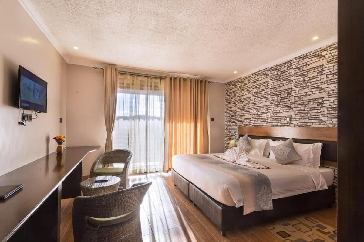 Habitación de hotel con una cama grande, un escritorio con silla, un televisor montado en la pared y una pared con diseño de piedra.