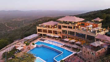 Un hotel de varios pisos con piscina, mobiliario exterior y vistas del paisaje circundante.