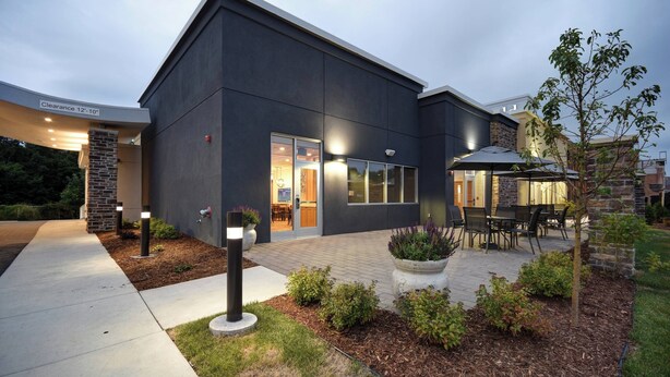 A modern building with a dark exterior, a covered patio area with outdoor seating, and a clear sign indicating a 12'-10" clearance.