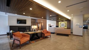 A lobby with a reception desk, a fireplace, two orange armchairs, a television, and a coffee station.