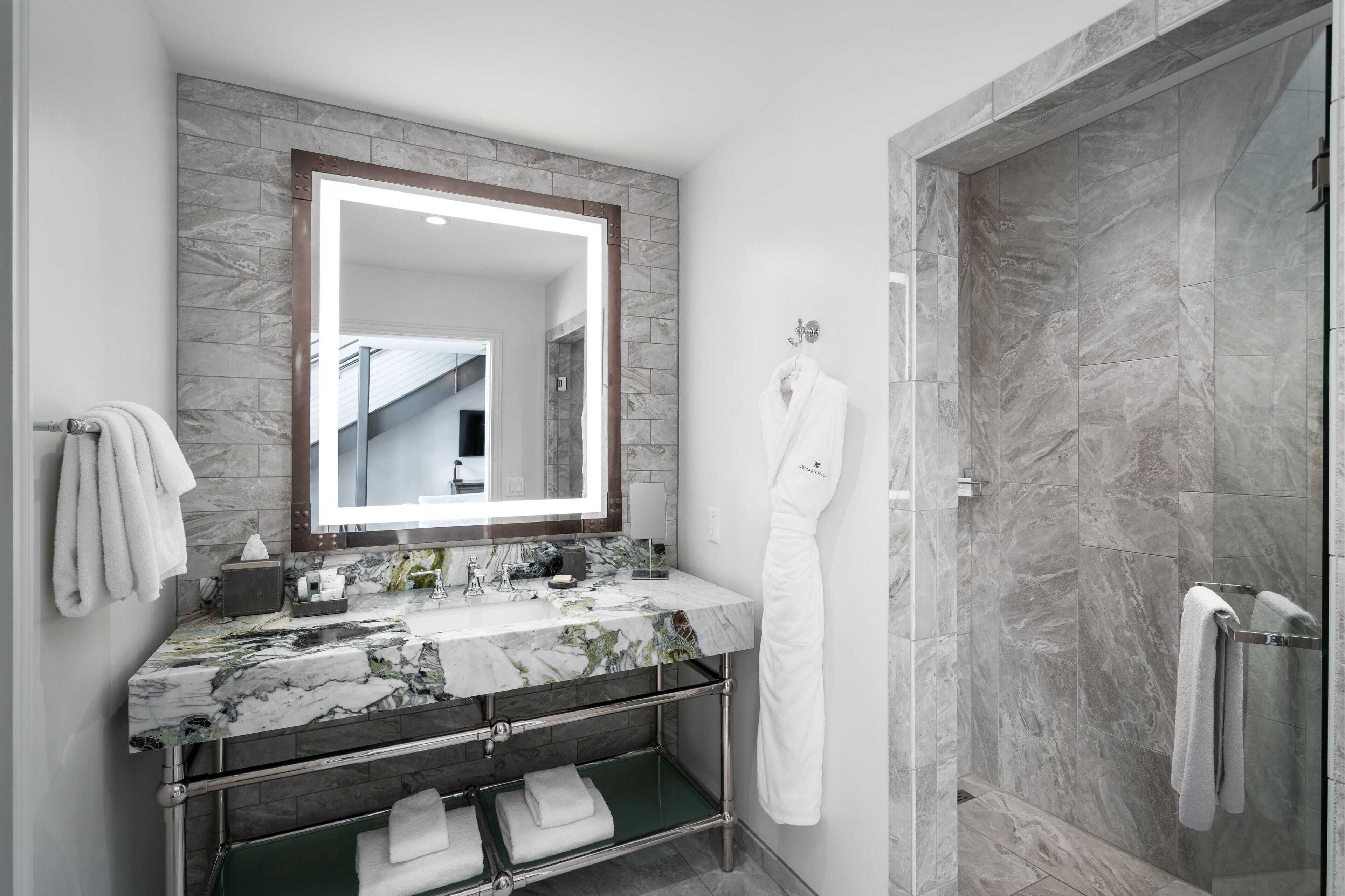 Une salle de bain moderne avec un lavabo en marbre, un grand miroir, une douche en verre et un porte-serviettes.