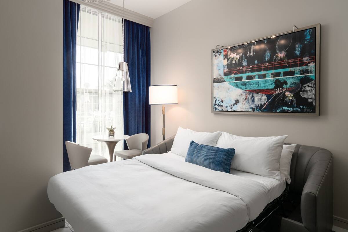 A hotel room with a large bed, a desk, a chair, a lamp, and a painting on the wall.