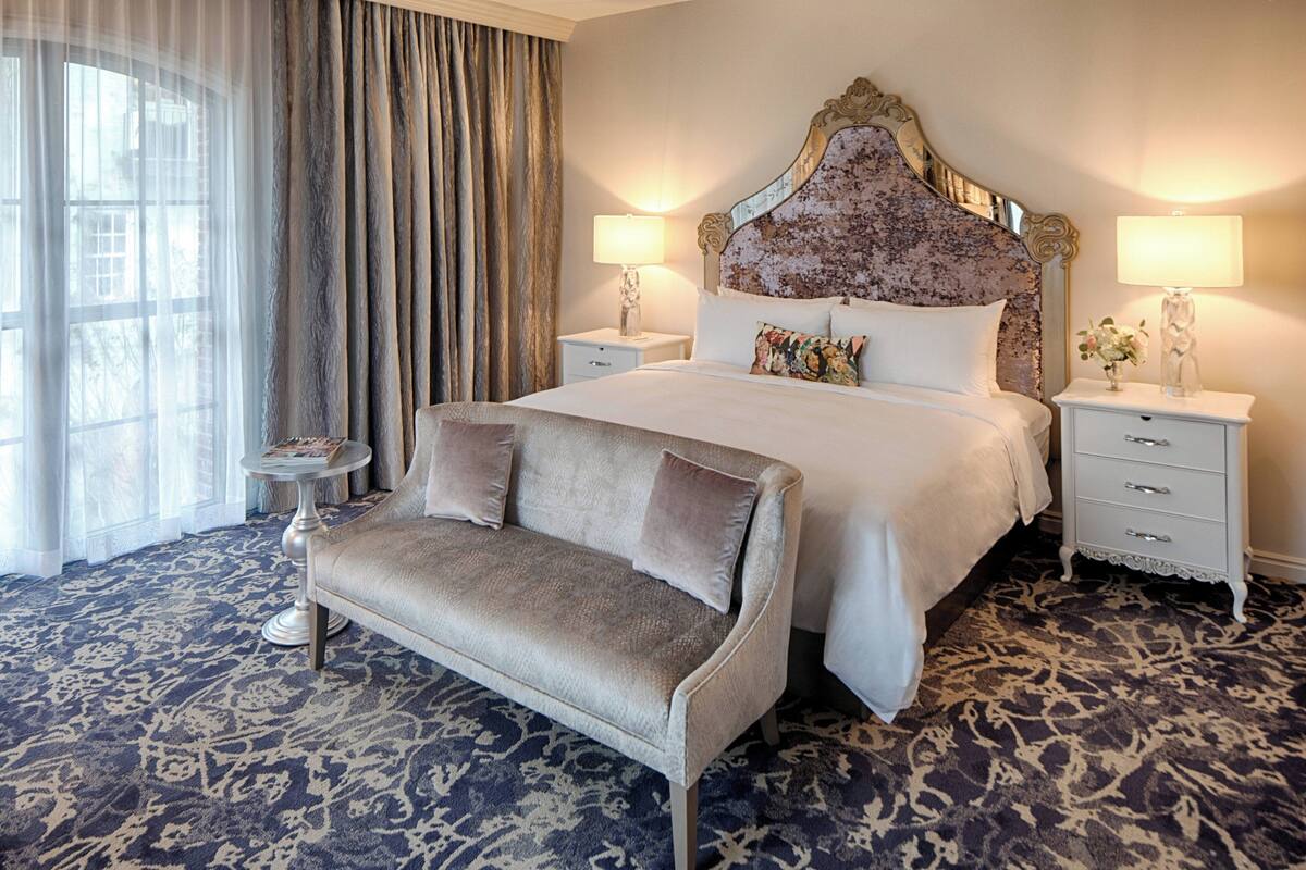 A hotel room with a large bed, two bedside tables, a sofa, and a patterned carpet.